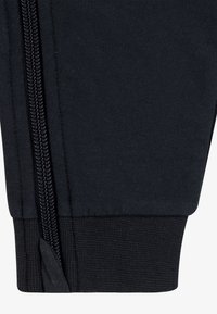 Svart joggebukse i bomull med mansjett som har en jevn tekstur, glidelåslukking og ribbestrikket kant. Detaljert søm langs sømmen.