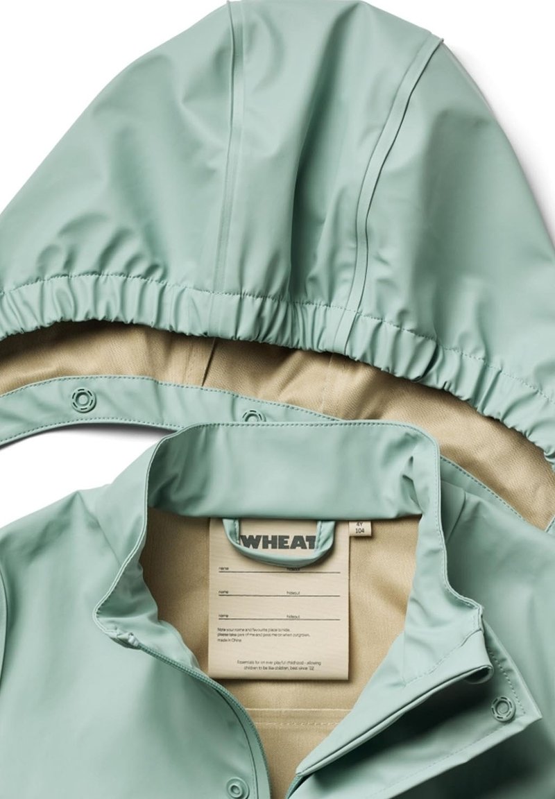 Veste légère vert menthe avec capuche, fermetures à pression et doublure intérieure beige avec une étiquette d'entretien à l'intérieur du col.