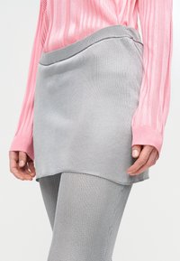 Γκρι πλεκτή φούστα με ομαλή υφή, σετ με αντίστοιχες γκρι καλσόν με ριπ υφή και ροζ μπλούζα με μακριά μανίκια και κάθετες ρίγες.