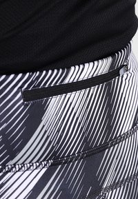 Legginsy w czarno-białe wzory z wąską kieszonką na zamek z tyłu, z diagonalnymi liniami i kontrastującą teksturowaną tkaniną.