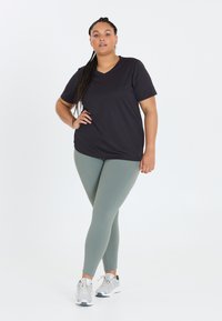 Sort kortærmet V-hals t-shirt parret med lysegrønne leggings. Model iført grå sneakers. Glat stof med en tætsiddende design.