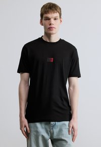 Μαύρο βαμβακερό t-shirt με στρογγυλή λαιμόκοψη, διαθέτει μικρό κόκκινο και μαύρο λογότυπο στο στήθος. Κοντά μανίκια και άνετη εφαρμογή.