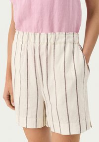 Lightweight, cream-colored shorts with vertical dark stripes, an elastic waistband, and side pockets. Made from breathable fabric.