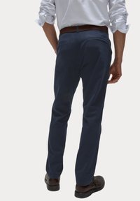 Pantaloni blu navy in tessuto morbido, con due tasche posteriori e vestibilità su misura, indossati con scarpe eleganti marroni.