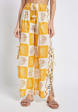 Weite Hosen in Creme mit gelb-braunem Muschelprint. Sie verfügen über einen Kordelzugbund und seitliche Schnürungen und sind aus leichtem Stoff gefertigt.