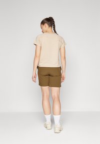 Beige t-skjorte med korte ermer og rund halsutskjæring, sammen med olivengrønne shorts, hvite ankelstrømper og lyse sneakers.