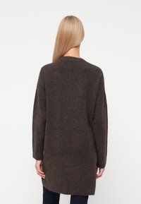 Cardigan long, marron foncé en maille avec un col rond, des manches longues et une coupe décontractée, offrant une texture douce et une longueur sous les hanches.