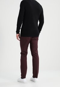 Haut à manches longues noir texturé associé à un pantalon bordeaux et à des baskets blanches, mettant en avant un design simple et des lignes épurées.