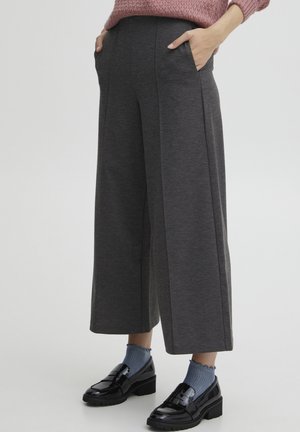 Grijze wijde broek met zijzakken, gemaakt van zachte stof. Draagt met blauwe sokken en zwarte lakleren instappers. Heeft een gladde textuur.