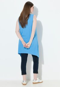 Túnica azul sin mangas, de corte holgado, combinada con leggings azul marino con ribete de encaje en el dobladillo y zapatillas blancas con detalles plateados.