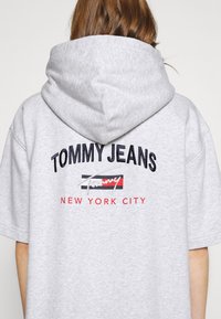 Šedá, převelká mikina s kapucí s velkým vyšívaným logem "TOMMY JEANS" a "NEW YORK CITY" v námořnické modré a červené barvě, texturovaná látka.