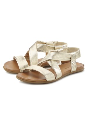 Goldfarbene metallische Sandalen mit überkreuzten Riemen, einer flachen braunen Sohle und einer glatten Textur. Sie verfügen über mehrere elastische Bänder für zusätzlichen Komfort.