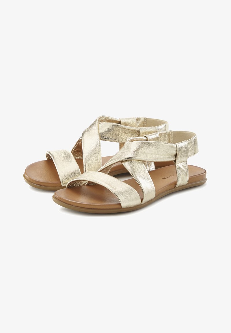 Gouden metalen sandalen met kruislings banden, een platte bruine zool en een gladde textuur. Voorzien van meerdere elastische banden voor extra comfort.