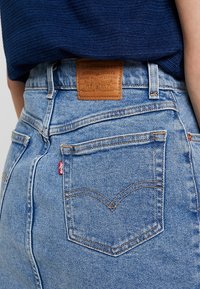 Vaaleansiniset farkut, joissa on korkea vyötärö, takana nahkainen etiketti ja klassiset ompelumallit taskuissa.