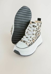 Sneakers w wysokim obcasie w panterkę z białą osłoną na palce, białymi sznurowadłami i grubą czarną podeszwą z poziomymi rowkami.