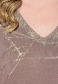 Pull en V couleur mauve avec des motifs abstraits dorés métalliques. Texture douce avec un léger scintillement au niveau du col et du tissu.