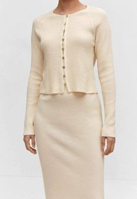 Pystyraitainen, kermaan vivahtava neuletakki pyöreällä pääntiellä ja viiden napin kiinnityksellä, yhdistettynä polveen ulottuvaan, samanlaiseen pystyraitaseeliseen vartalonmyötäiseen mekkoon.