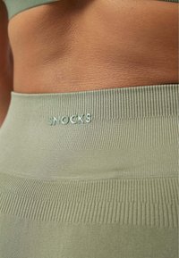 Fascia in verde khaki con texture a coste, con un sottile logo "SNOCKS" in filo coordinato. Materiale liscio con un design aderente.