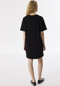 Zwart katoenen t-shirt jurk met een relaxte pasvorm, korte mouwen en een rechte zoom. Geen zichtbare patronen of versieringen.