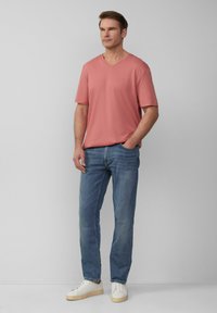 Jasnoróżowa koszulka z dekoltem w serek o luźnym kroju, w połączeniu z wyblakłymi niebieskimi dżinsami o prostym kroju i białymi trampkami z beżowymi podeszwami. Prosty design, bez wzorów.