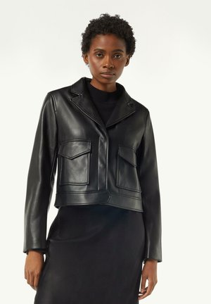 Schwarze kurze Lederjacke mit eingekerbten Revers, zwei Fronttaschen und glatter Textur. Getragen über einem schwarzen Pulloverkleid.