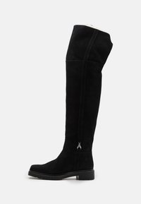 Botas negras de ante por encima de la rodilla, con un ligero tacón, cremallera lateral con un charm decorativo y un diseño elegante y suave.