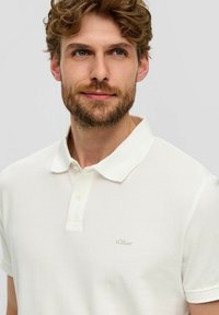 Weißes Poloshirt aus texturiertem Stoff, mit einem knöpfbaren Kragen und kleinem, in heller Farbe gesticktem Logo auf der Brust.