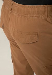 Braune Cargo-Hosen verfügen über einen elastischen Bund, eine Rückentasche mit dekorativer Naht und eine glatte Stoffstruktur.