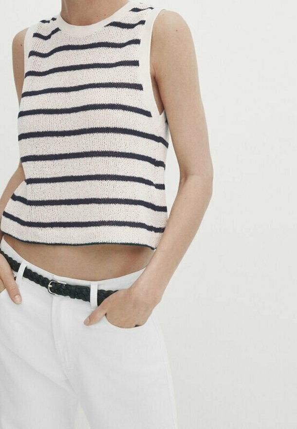 Sweter zakrywający brzuch w kolorze kremowym z granatowymi poziomymi paskami. Bez rękawów, z okrągłym dekoltem i prążkowanymi krawędziami. W zestawie z białymi spodniami.