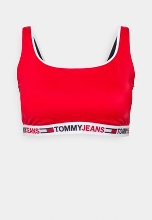 Sutiã desportivo vermelho com uma textura suave, alças largas e uma faixa branca com o logótipo "TOMMYJEANS" em preto e vermelho.