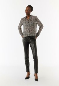 Camicia con stampa leopardata nei toni del beige e del nero, abbinata a pantaloni in finta pelle nera e scarpe col tacco nere. Texture complessiva liscia.
