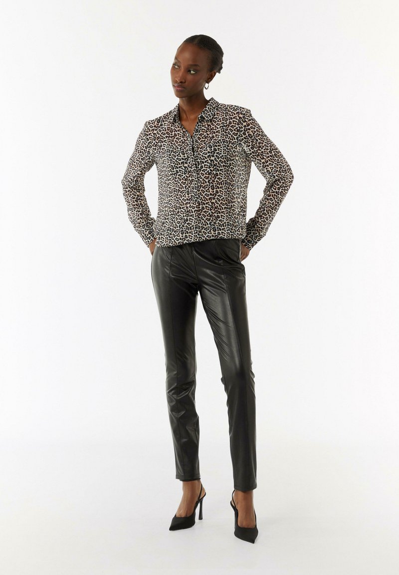 Camicia con stampa leopardata nei toni del beige e del nero, abbinata a pantaloni in finta pelle nera e scarpe col tacco nere. Texture complessiva liscia.
