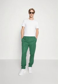 Πράσινη φόρμα με ελαστική μέση, συνδυασμένη με λευκό κοντομάνικο μπλουζάκι. Το μοντέλο φορά γυαλιά ηλίου και λευκά αθλητικά παπούτσια.