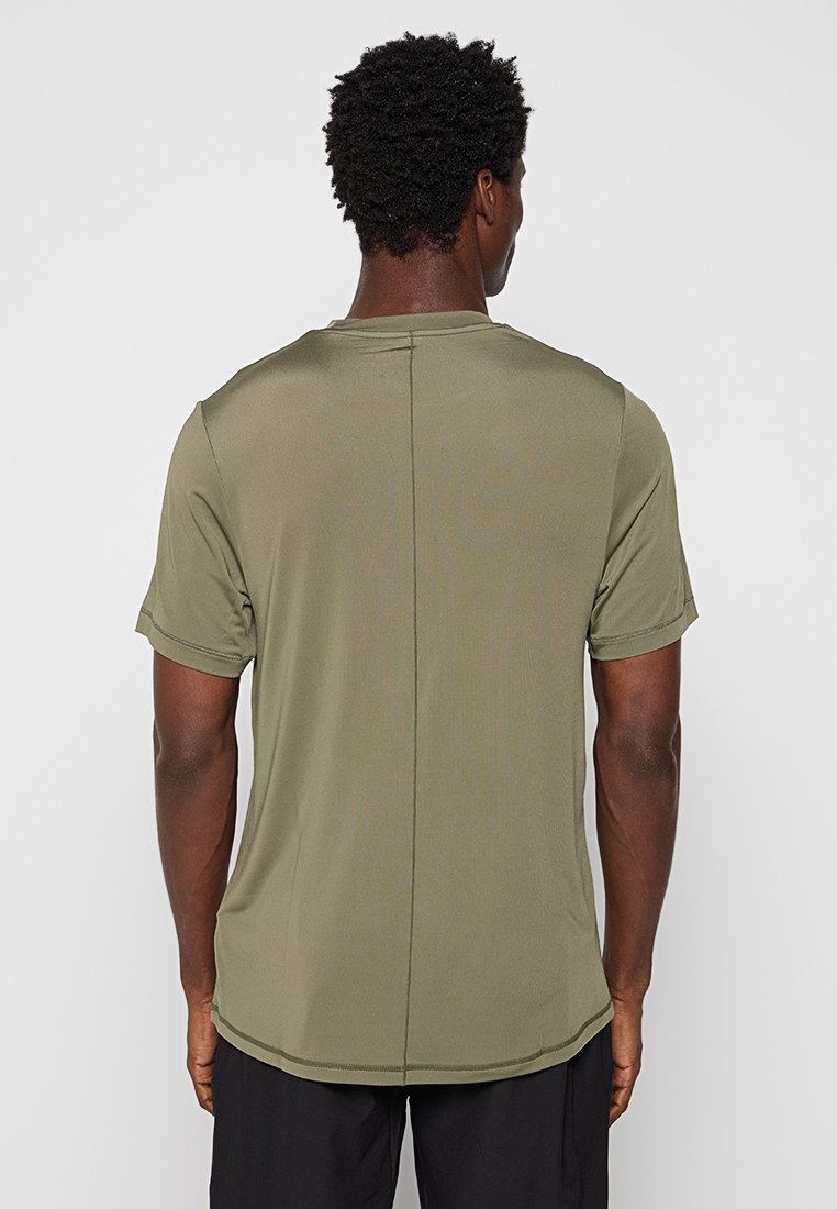 Camiseta atlética de manga corta en verde oliva con una textura suave, que presenta un detalle de costura central y un dobladillo redondeado en la parte posterior.