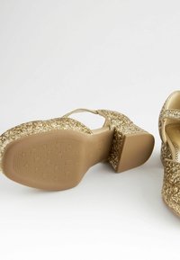 Goldene Glitzer-Plateauschuhe mit Blockabsatz und einer strukturierten Gummisohle. Das Design verfügt über einen T-Riemen und eine abgerundete Zehenpartie für Stabilität.