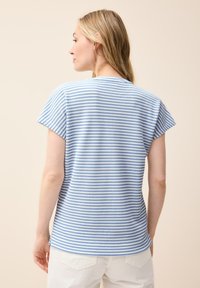 Camiseta de rayas azul y blanca con mangas cortas y cuello redondo. Tela texturada con un corte relajado, combinada con pantalones de color claro.