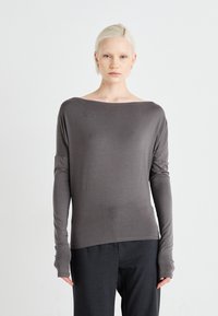 Gray long-sleeve top with a wide neck, soft texture, and fitted sleeves extending past the wrists, paired with dark trousers.