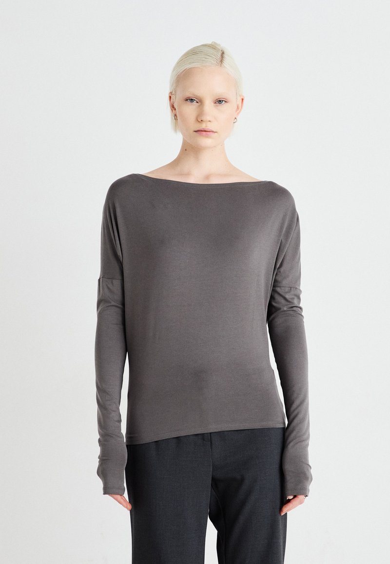 Gray long-sleeve top with a wide neck, soft texture, and fitted sleeves extending past the wrists, paired with dark trousers.