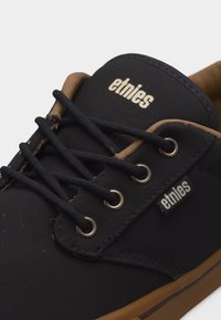 Μαύρο καμβαδένιο αθλητικό παπούτσι με καφέ διακόσμηση, μαύρα κορδόνια, μεταλλικές τρύπες για κορδόνια και λογότυπα "etnies" στη γλώσσα και στην πλαϊνή ετικέτα.
