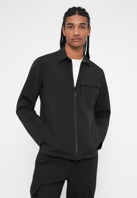 Črna zip-jakna s ovratnikom, žepom na prsih in elegantnim dizajnom. Narejena iz lahkega materiala z gladko teksturo.
