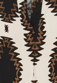 Svart och brunt zickzackmönster på krämfärgad tyg som bildar en symmetrisk, stam-inspirerad design runt en V-formad halsringning.
