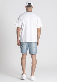 Biela, krátkotrvajúca tričko s krátkym rukávom skombinované s modrými džínsovými šortkami s vreckami, doplnené bielymi teniskami a bielou čiapkou.