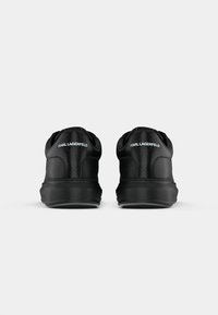 Sapatos atléticos pretos com um traseiro texturizado, corpo liso e detalhe do logotipo. Bico arredondado e colarinho acolchoado para conforto.