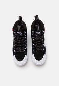 Černé vysoké tenisky vyrobené z materiálů suede a plátno, s bílou gumovou podrážkou, černými textilními tkaničkami a charakteristickým brandingem Vans.