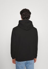 Černá mikina s velkou kapucí, ribbenými manžetami a lemem, vyrobená z měkkého materiálu. Nositelná přes světle modré džíny, s jednoduchým, neformálním designem.