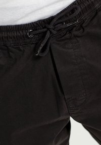 Pantalones con cintura elástica negra y cordón ajustable. Tienen una textura suave y un bolsillo lateral. Las costuras son visibles.