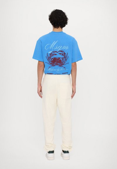 Blue cotton t-shirt with a large red crab graphic on the back, paired with cream tapered sweatpants and green-accented sneakers.