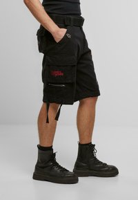 Sorte cargo-shorts med flere lommer, lynlåsdetalj og justerbare snorer. Kombinert med svarte militærstøvler. Laget av bomull.