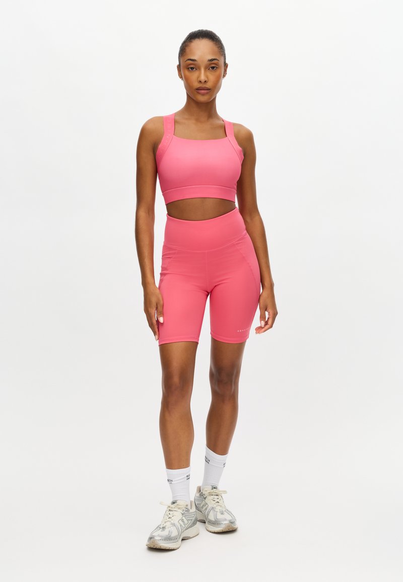 Top sportivo corto rosa e shorts a vita alta, realizzati in materiale elastico, con una sezione centrale traforata. Texture trasparente e liscia con pochi dettagli.
