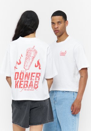 Deux personnes portant des t-shirts blancs avec le texte rouge "Döner Kebab" et un graphisme de brochette de viande ; l'une fait face vers l'avant, l'autre montre le design arrière.
